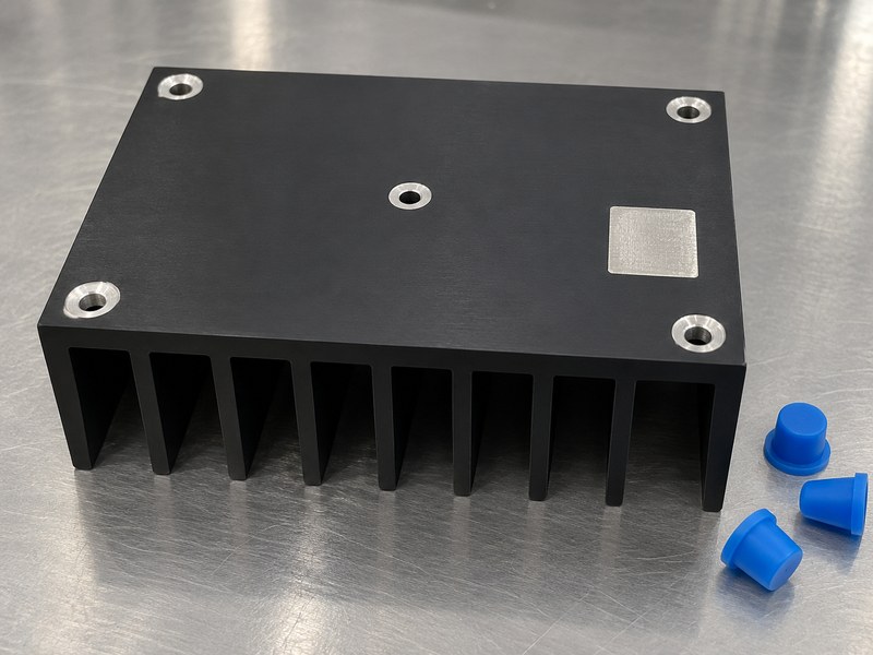 machined anodized aluminum heat sink: bare mounting features on a black heat sink beside separate masking plugs